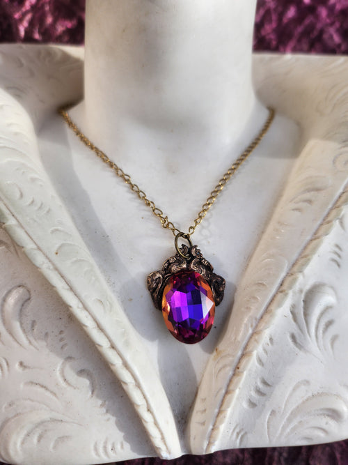 Colección Resonancia Arcana – Colgante artesanal de bronce con cristal ovalado morado, fucsia y ámbar.